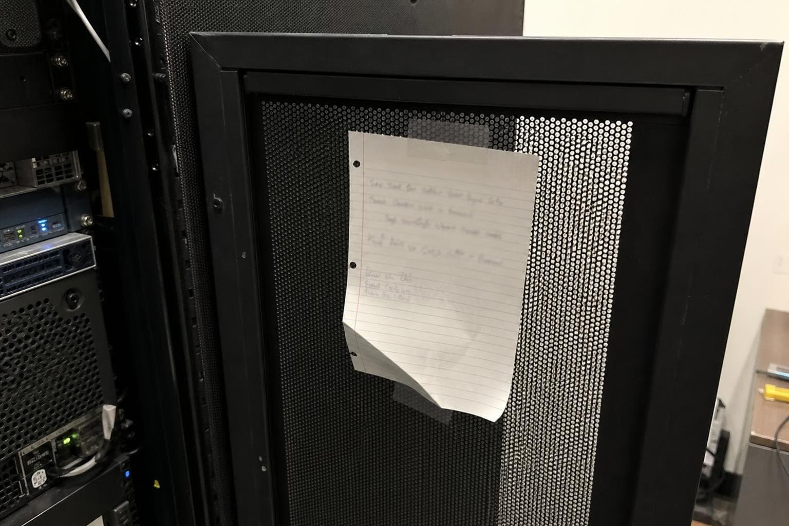 A handwritten note taped inside a server rack door, edges curling.