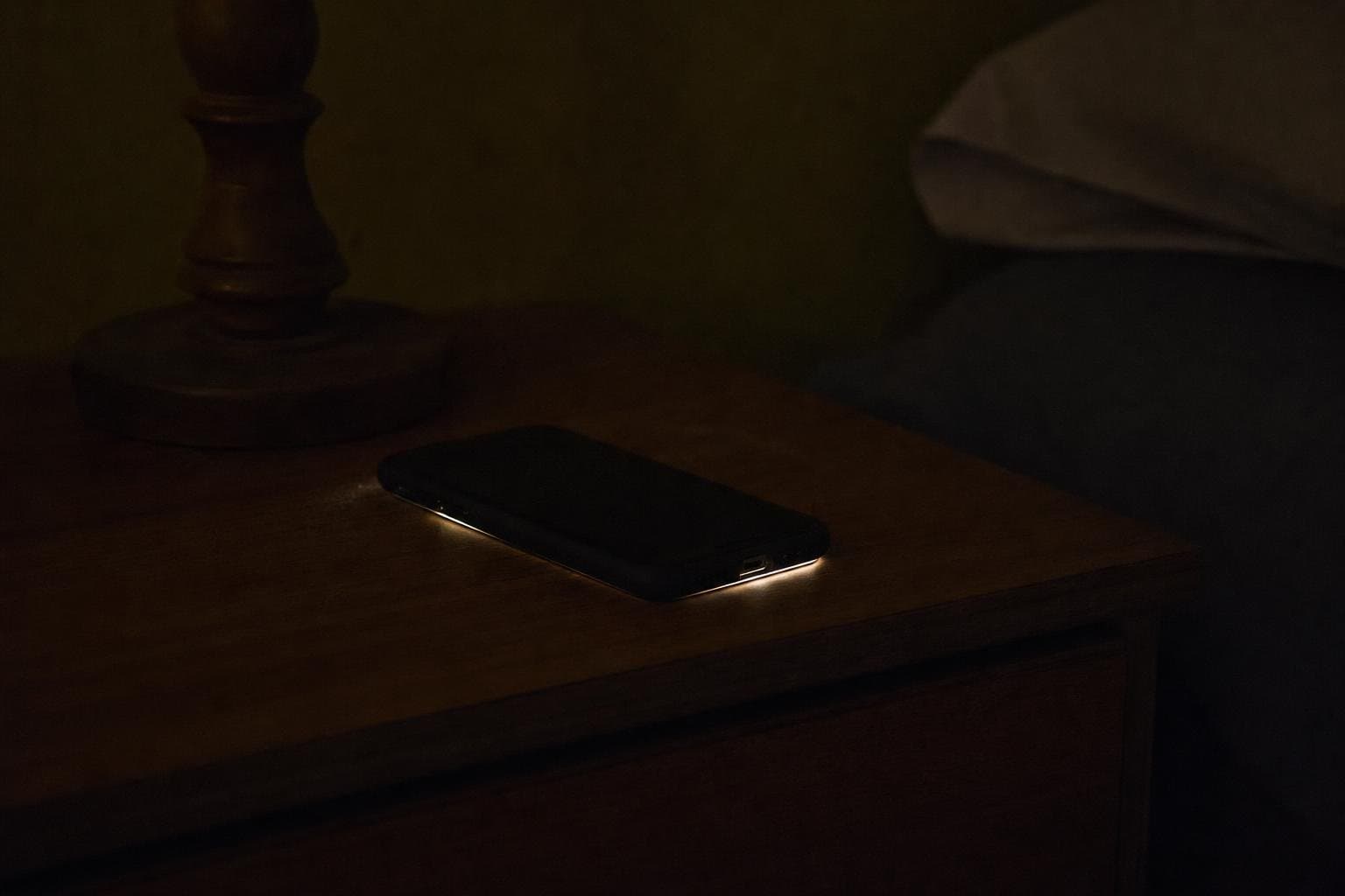 A phone glowing face-down on a nightstand in a dark room at night.
