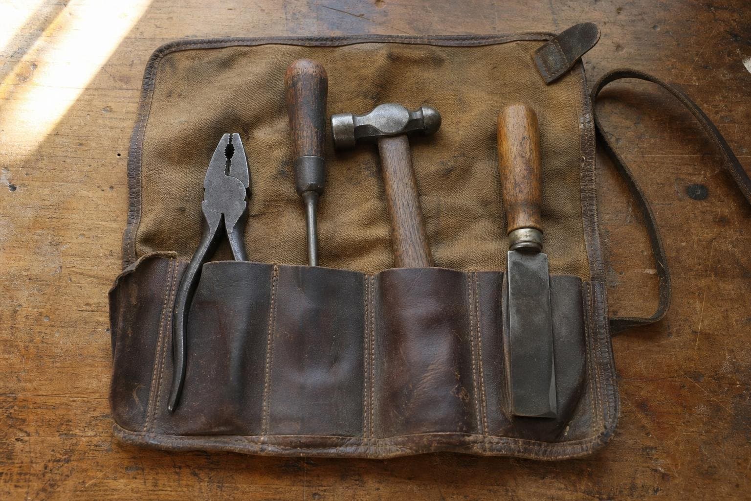 A small tool roll open on a workbench with only a few essential tools inside.