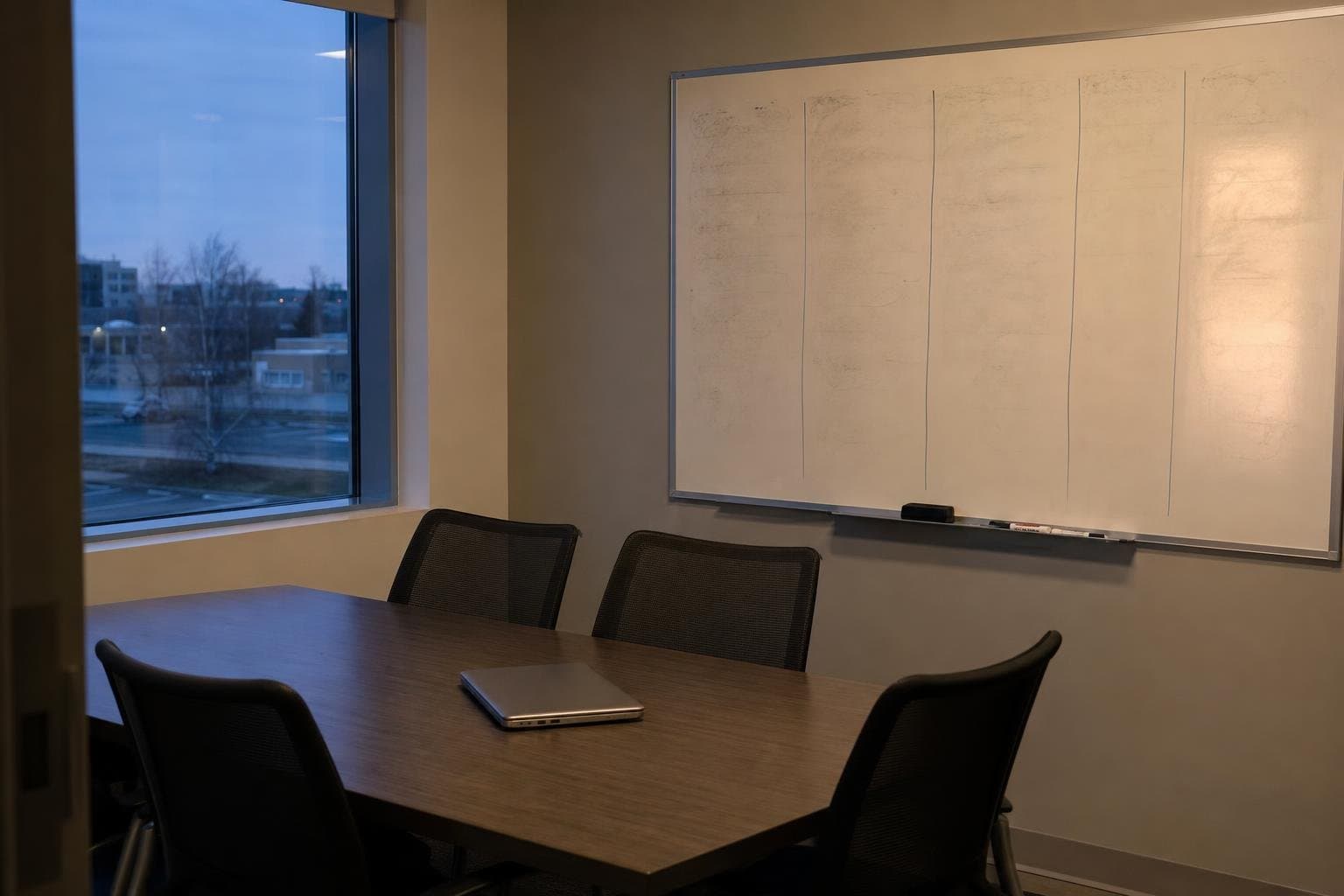 An empty office meeting room with a faded whiteboard and a closed laptop, evening light.