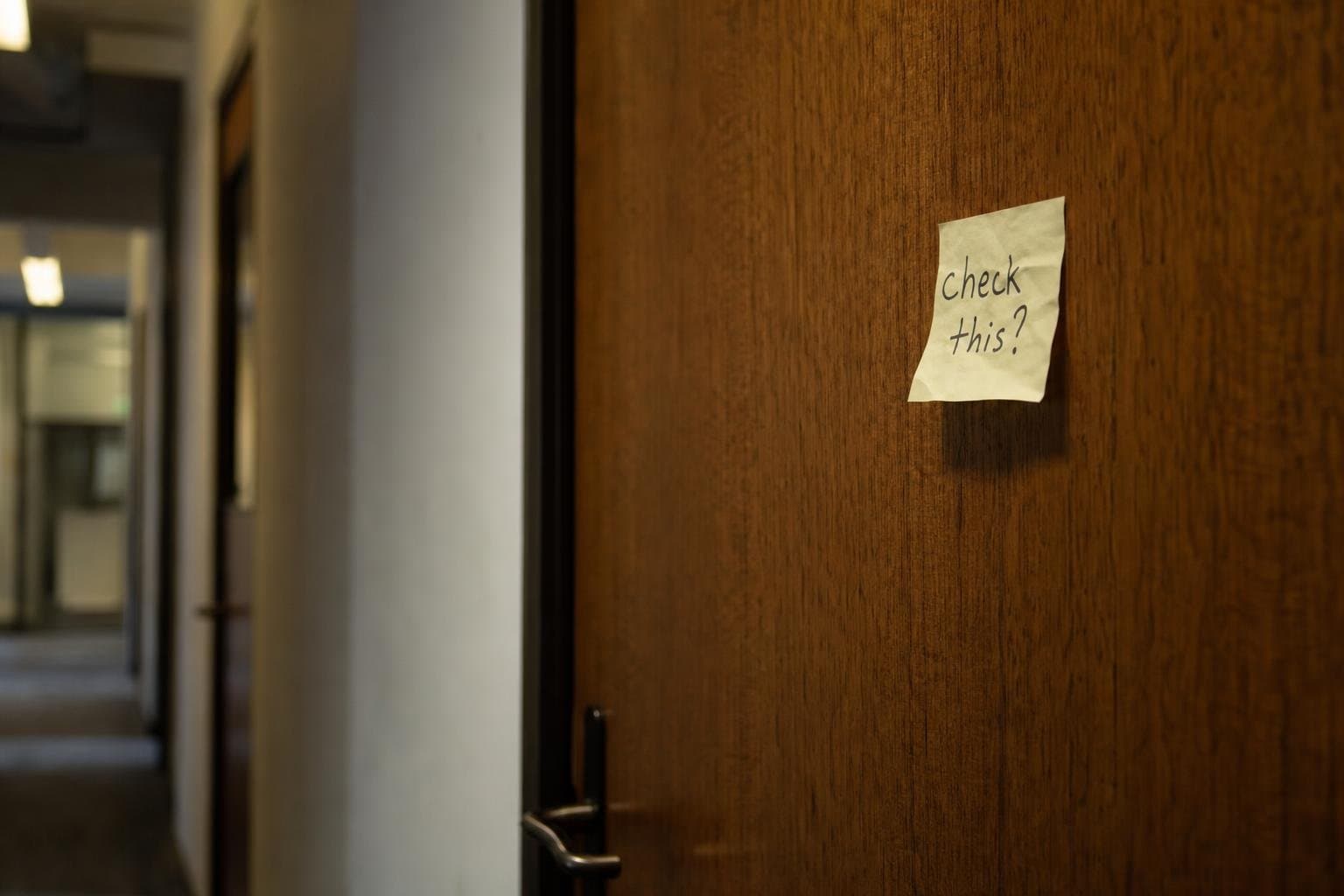 A crumpled note reading a vague question stuck to a closed office door.