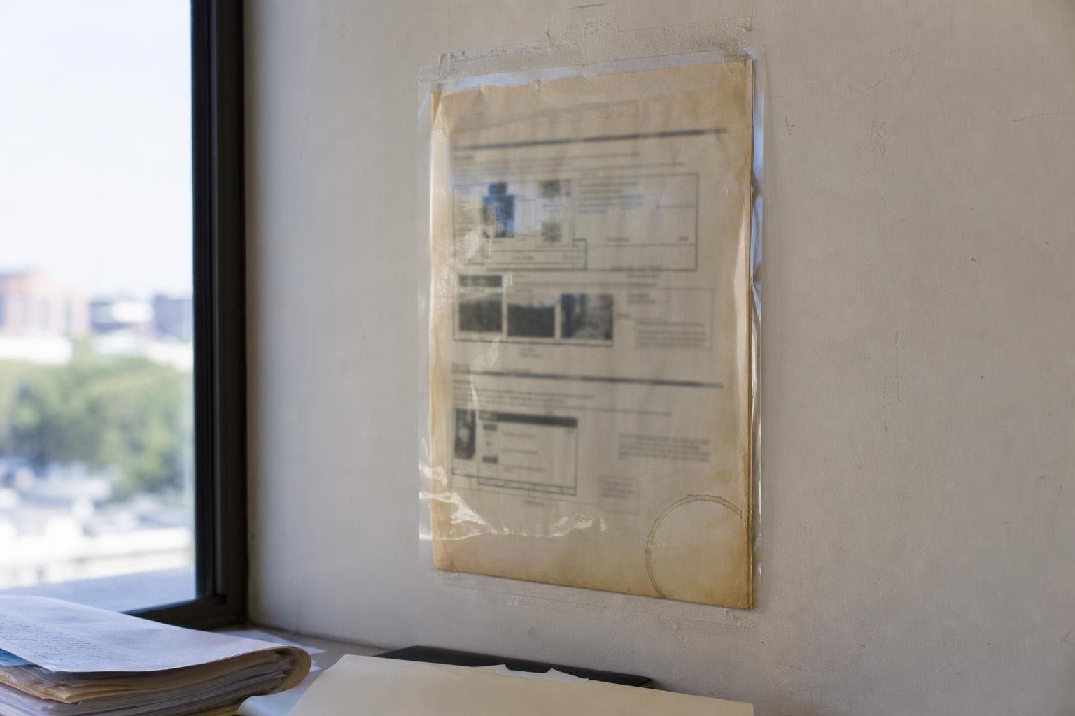 A curling, yellowed laminated instruction sheet taped to a wall above a workspace.