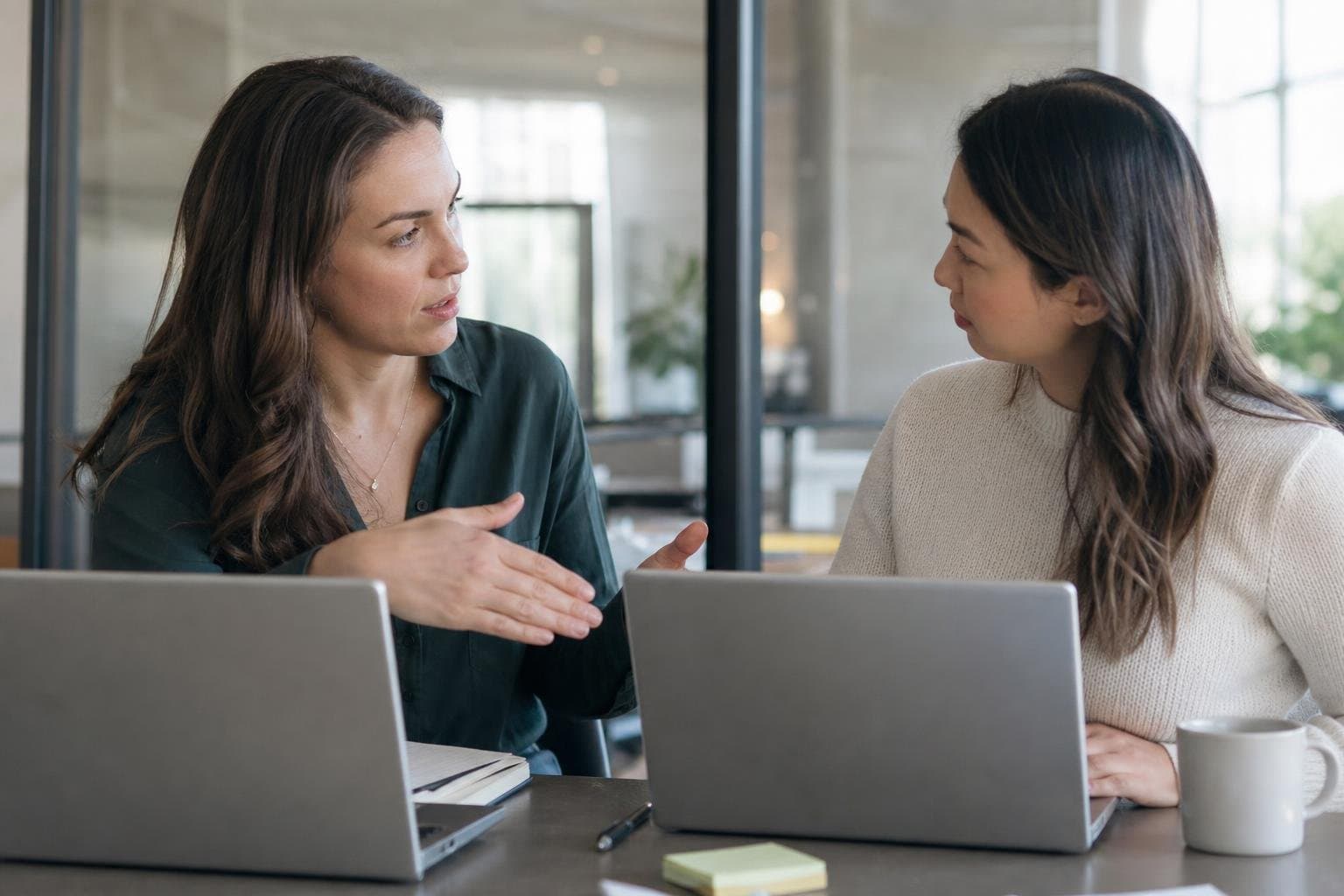 Two coworkers in a handoff conversation at a small office table