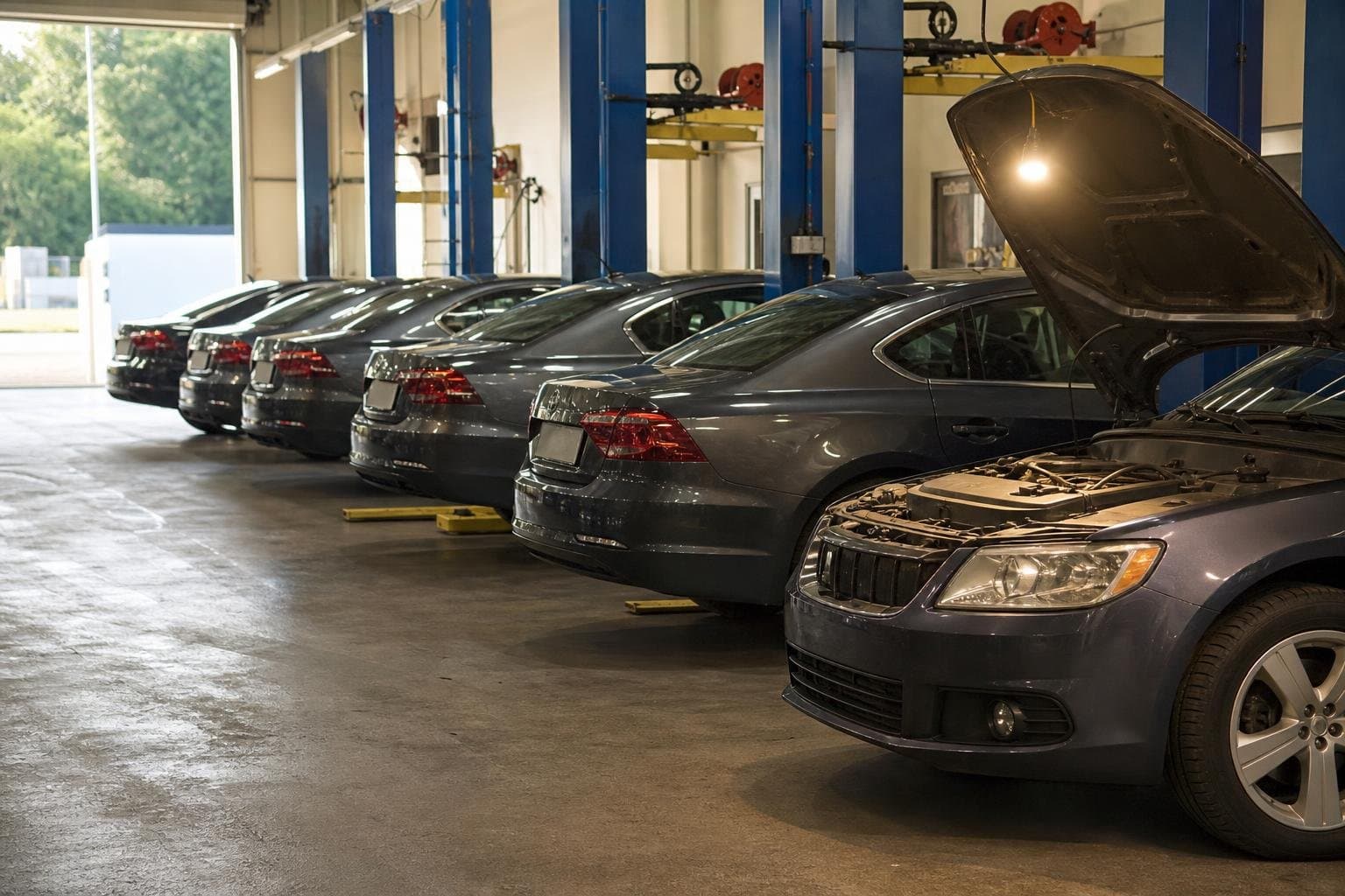 Four identical cars in a row for routine service, with one pulled aside under a work light for extra attention.