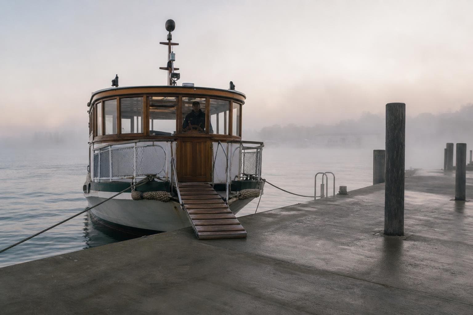 A ferry with its gangplank down waiting at an empty dock in the fog, no passengers yet aboard.