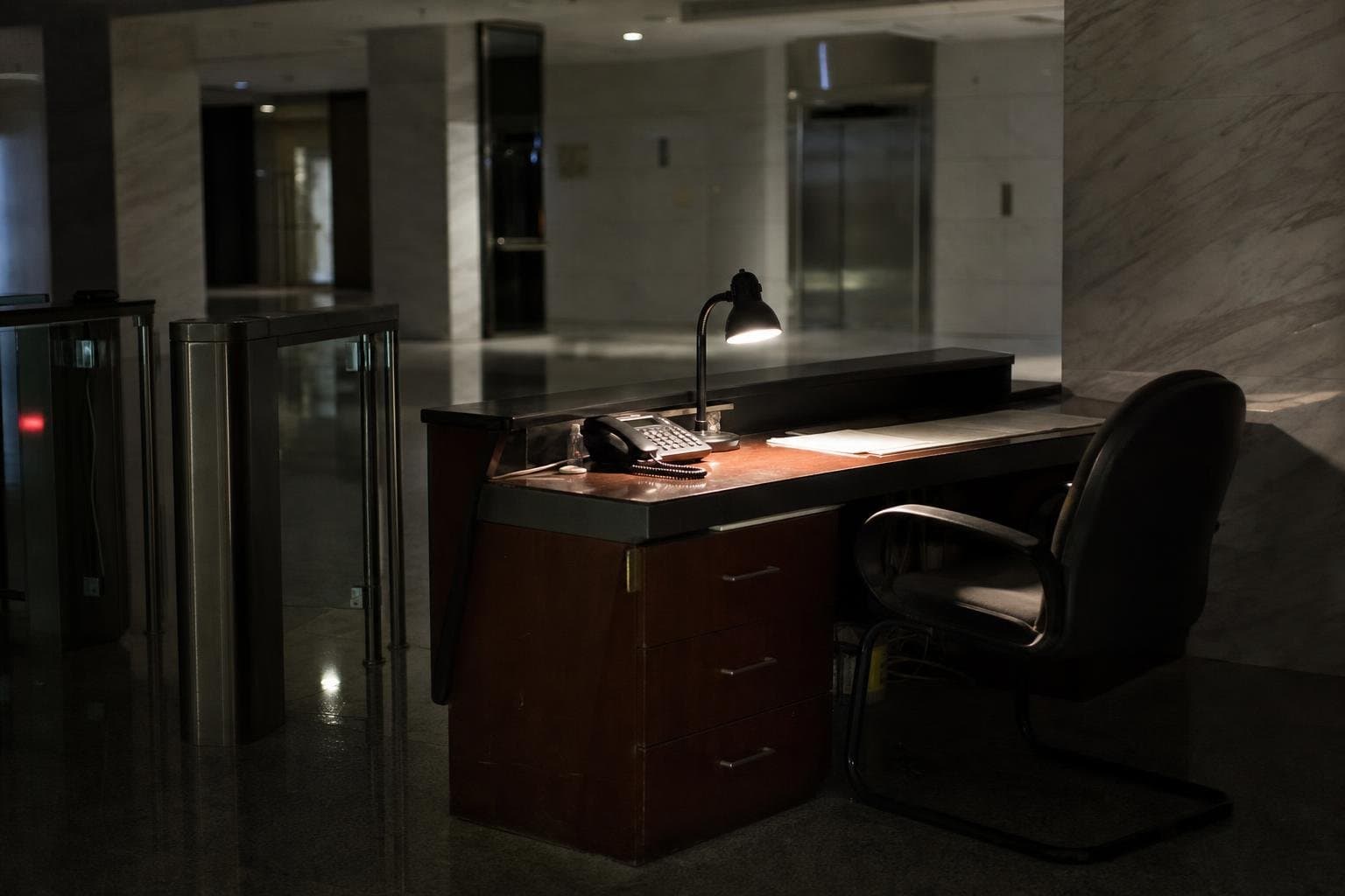 An empty chair at an unattended desk, lit by a single lamp at night.